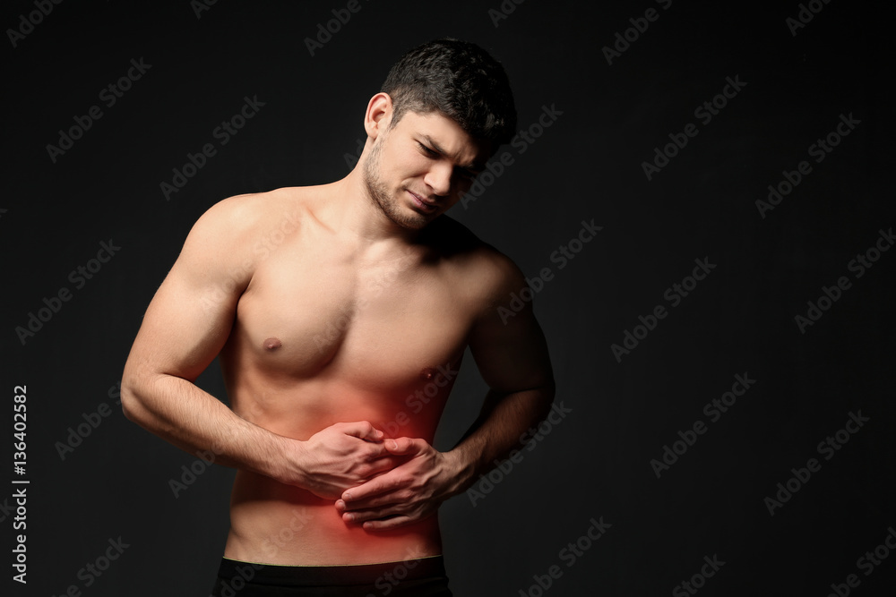 Young man suffering from abdominal pain on black background. Health care concept Young man suffering from abdominal pain on black background. Health care concept