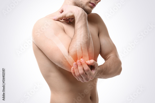 Young man suffering from elbow pain on light background. Health care concept photo