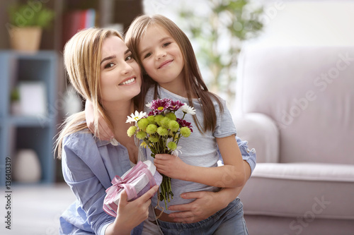 Beautiful young woman with present and bouquet of flowers from her daughter. Mother's day concept