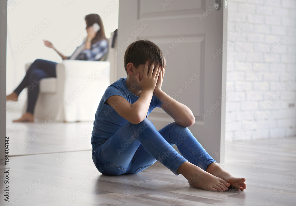 Fototapeta premium Sad little boy sitting on floor beside door