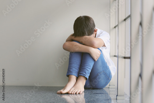 Sad little boy sitting beside wall
