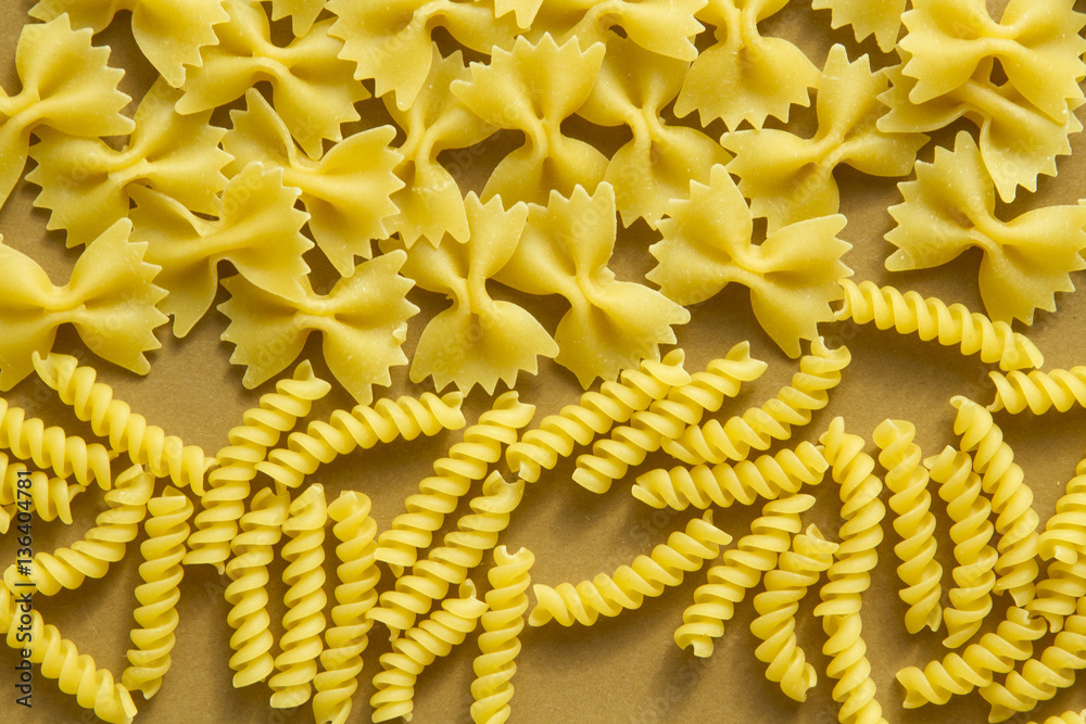 Bow and spiral shape pasta on brown background close view
