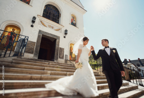 Newlyweds are walking down the stairs from the church