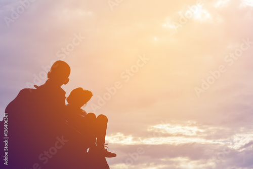 Silhouette of girl and boy on rock at the sky sunset