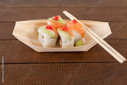 Four uramaki sushi served with chopsticks in wooden boat plate