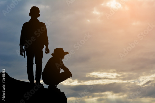 Silhouette of girl and boy on rock at the sky sunset