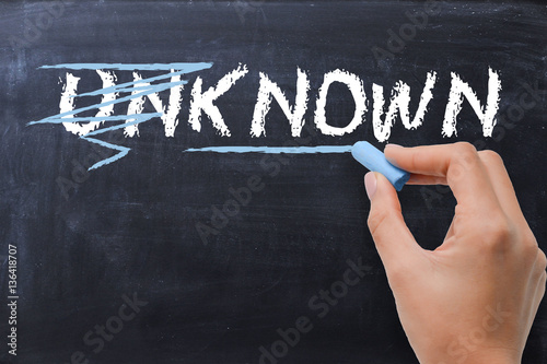 Woman changing the word unknown into known with chalk on blackboard photo