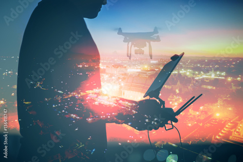 Man playing with the drone. Silhouette against the sunset sky and the cityscape background.