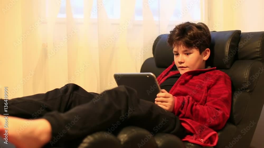 Child boy lying on a couch and using digital tablet computer Child boy lying on a couch and using digital tablet computer