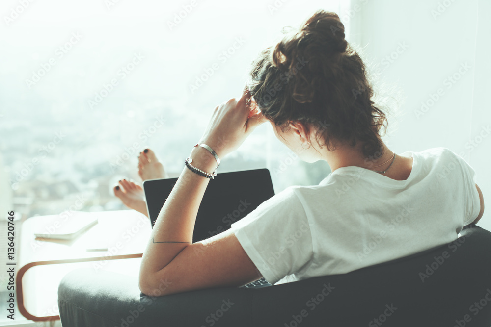 Young business woman sitting in her office workspace with laptop and big panoramic window