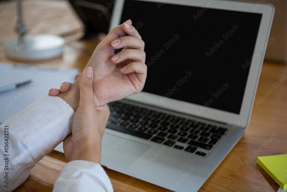 Female business executive holding her wrist near laptop