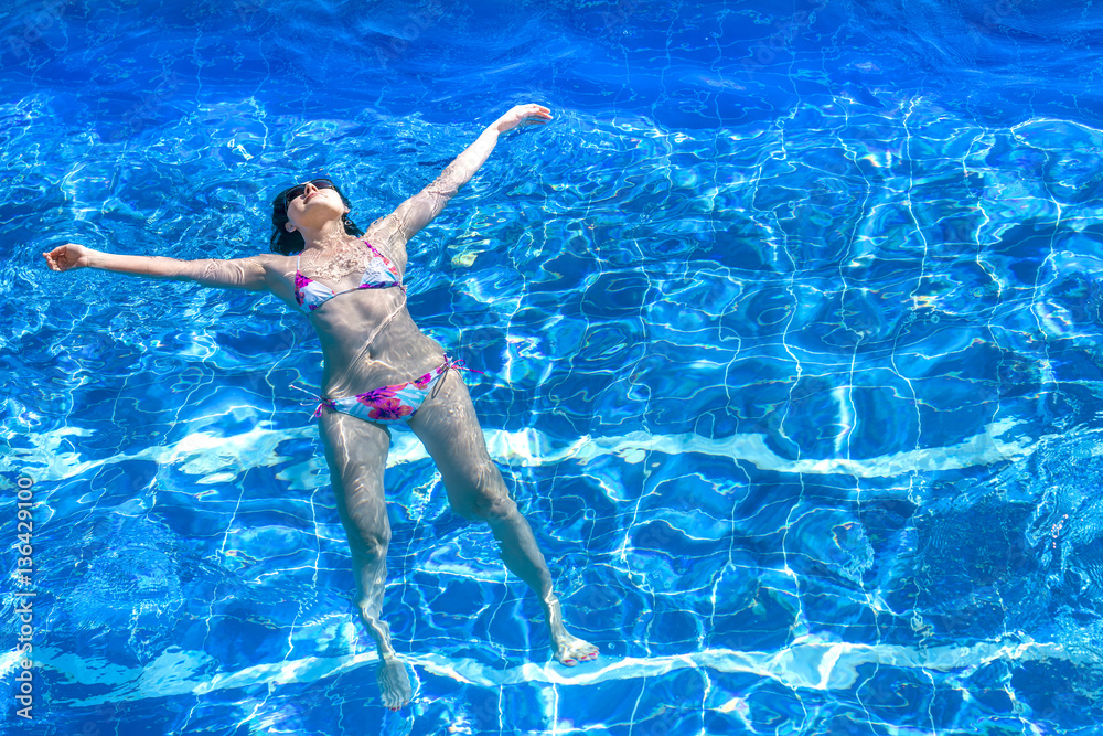 Woman in bikini and sunglasses lying in the water