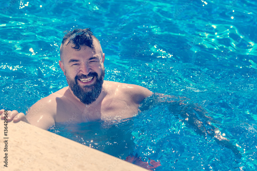 Bearded man with a a mohawk hairstyle in water near the edge of the pool Bearded man with a a mohawk hairstyle in water near the edge of the pool