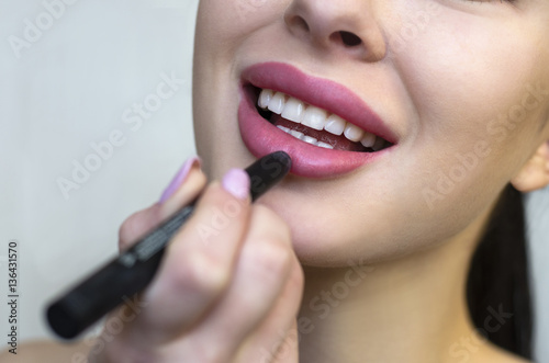 Woman putting makeup lipstick. Caucasian girl putting lip gloss pink lipstick smiling happy, close up.