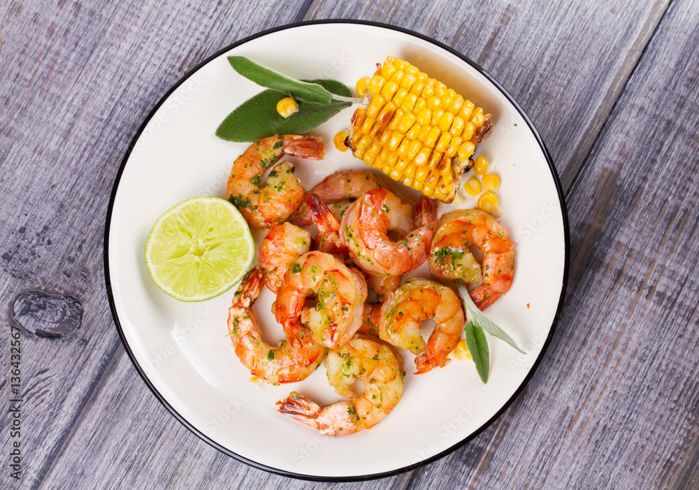 Grilled shrimps and corn garnished with lime and sage leaves. Prawns on white plate. View from above, top studio shot Grilled shrimps and corn garnished with lime and sage leaves. Prawns on white plate. View from above, top studio shot