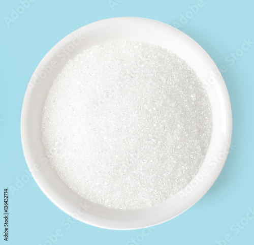 Bowl of sugar on blue background, top view