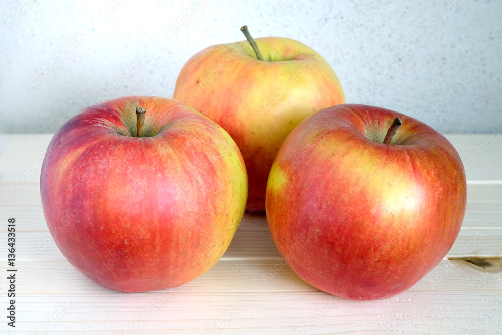 Three big ripe apples on wooden shelf indoor front view closeup
