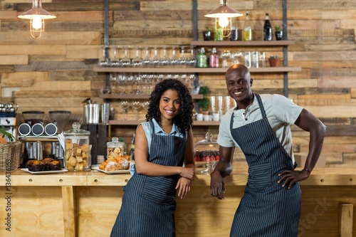 Portrait of smiling waiter and waitress leaning at counter