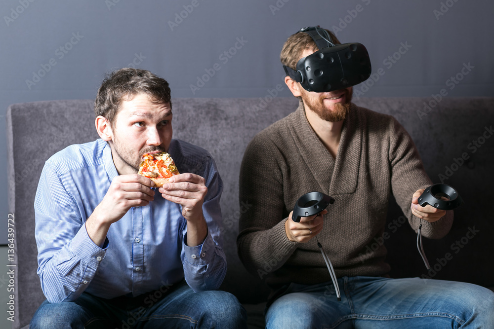man using virtual reality headset and his friend eat pizza man using virtual reality headset and his friend eat pizza