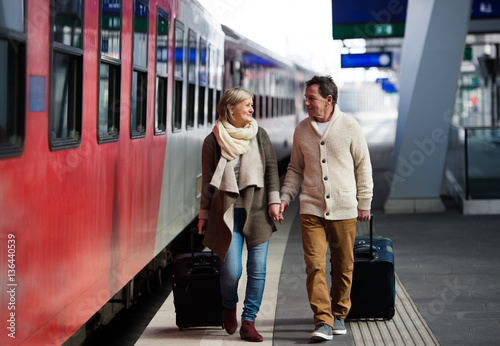 Senior couple on train station pulling trolley luggage.