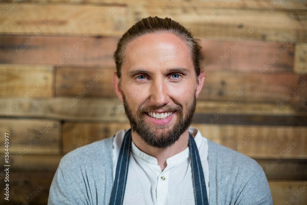 Portrait of smiling waiter standing against wooden wall