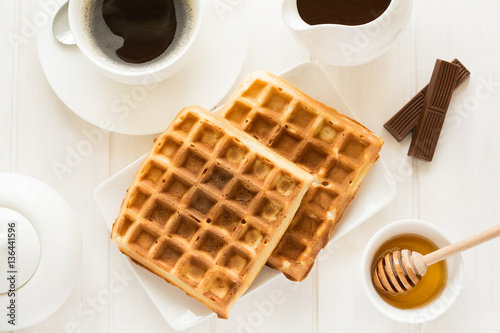 Traditional breakfast: coffee, belgian waffles with honey and chocolate sauce on white wooden table. Selective focus