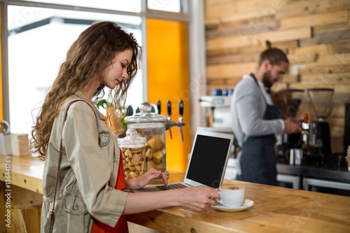 Woman standing at counter and using laptop while having coffee