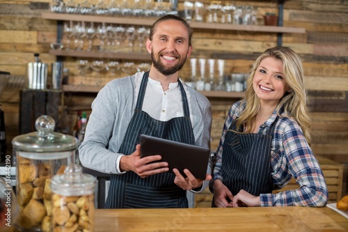 Smiling waiter and waitress using tablet at counter 