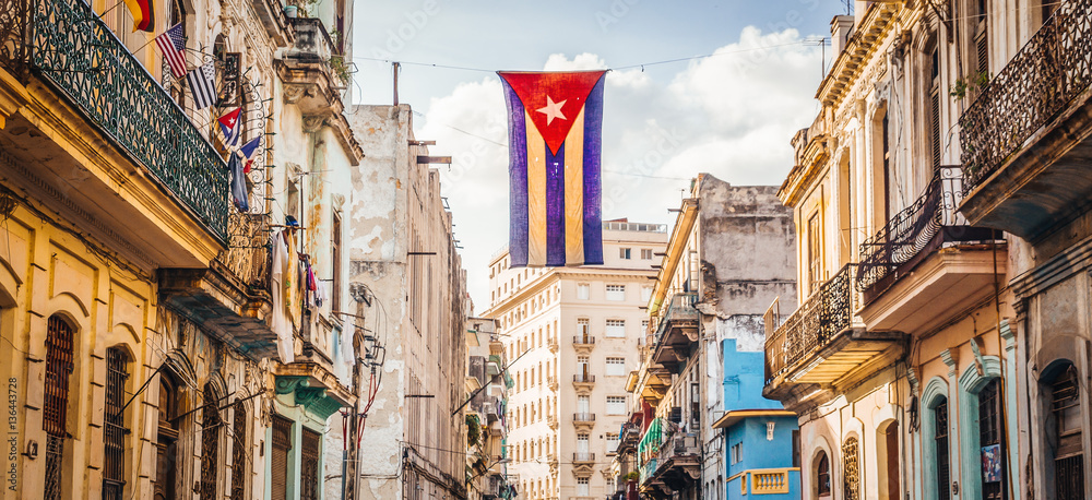Naklejka premium Kubańska flaga z dziurami faluje nad ulicą w Central Havana. La Habana, jak nazywają to miejscowi, jest stolicą Kuby