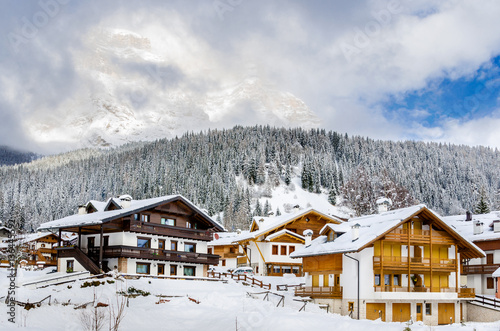 Beautiful Alpine Village Covered in Snow with a Woody Mountain in Background.