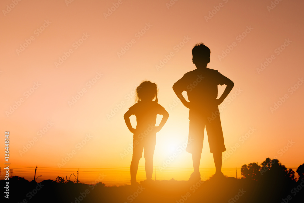 Silhouettes of boy and girl playing at sunset evening sky background.