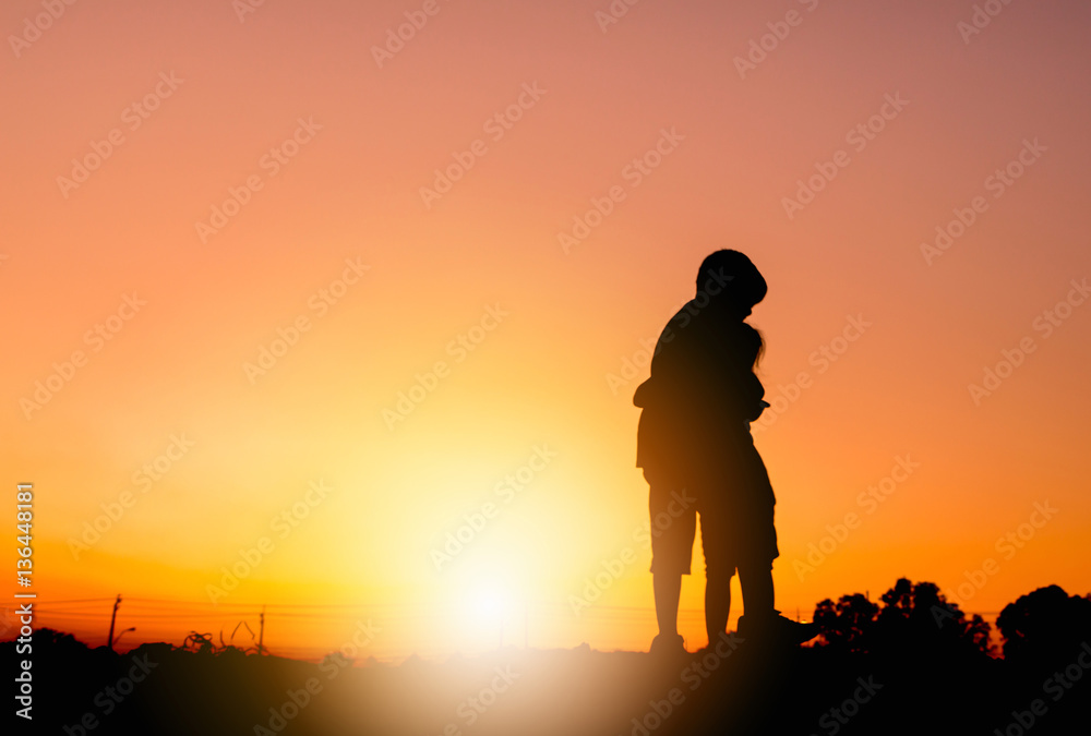 Silhouettes of boy and girl playing at sunset evening sky background.