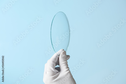 Scientist hand in glove show circle piece of new research prototype of transparent clear glass or plastic material