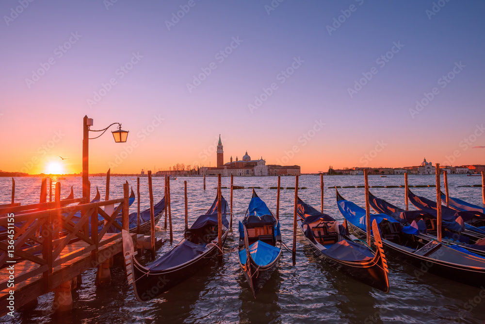 Gondolas moored to the poles in Europe Venice near the city center and Saint Mark square with a background view of the church of San Giorgio Maggiore at sunrise