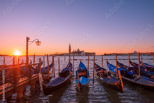 Gondolas moored to the poles in Europe Venice near the city center and Saint Mark square with a background view of the church of San Giorgio Maggiore at sunrise