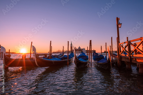 Italian gondolas moored to the poles in Europe Venice near the city center and Saint Mark square with a background view of the church of San Giorgio Maggiore at sunrise