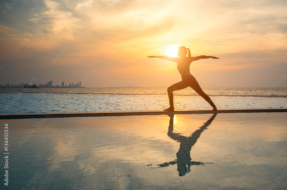 Silhouette young woman practicing yoga on swimming pool and the beach at sunset Silhouette young woman practicing yoga on swimming pool and the beach at sunset