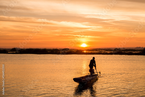 fisherman on long tail boat in the lake with sunrise background