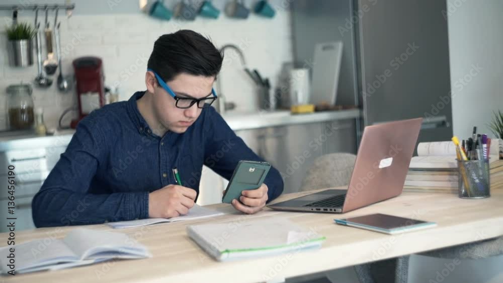 Young teenager doing homework with smartphone by the desk at home
Young teenager doing homework with smartphone by the desk at home