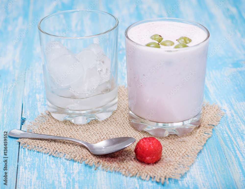 Milkshake with strawberries, gooseberries and ice on a blue table. Milkshake with strawberries, gooseberries and ice on a blue table.