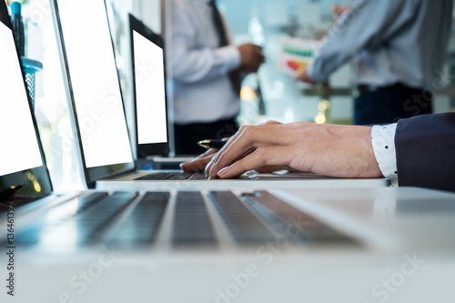 business man using laptop computer on office table with two partners interacting on background