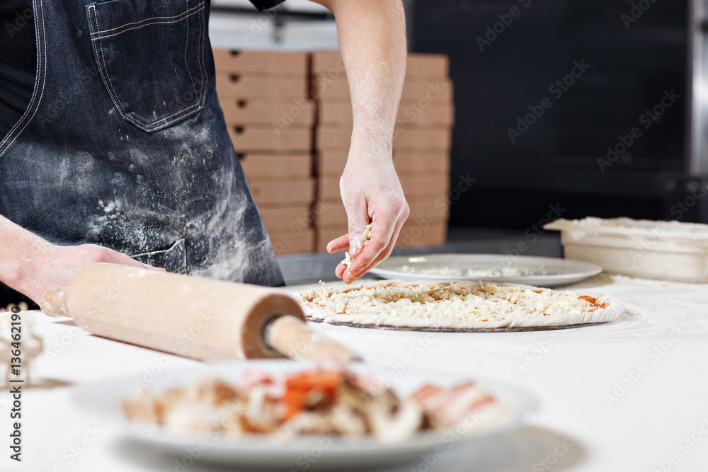 Cooking pizza. arranges cheese ingredients on the dough preform. Closeup hand of chef baker in uniform blue apron cook at kitchen