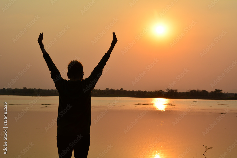 Woman put hand up beside lake under the sky and sun evening