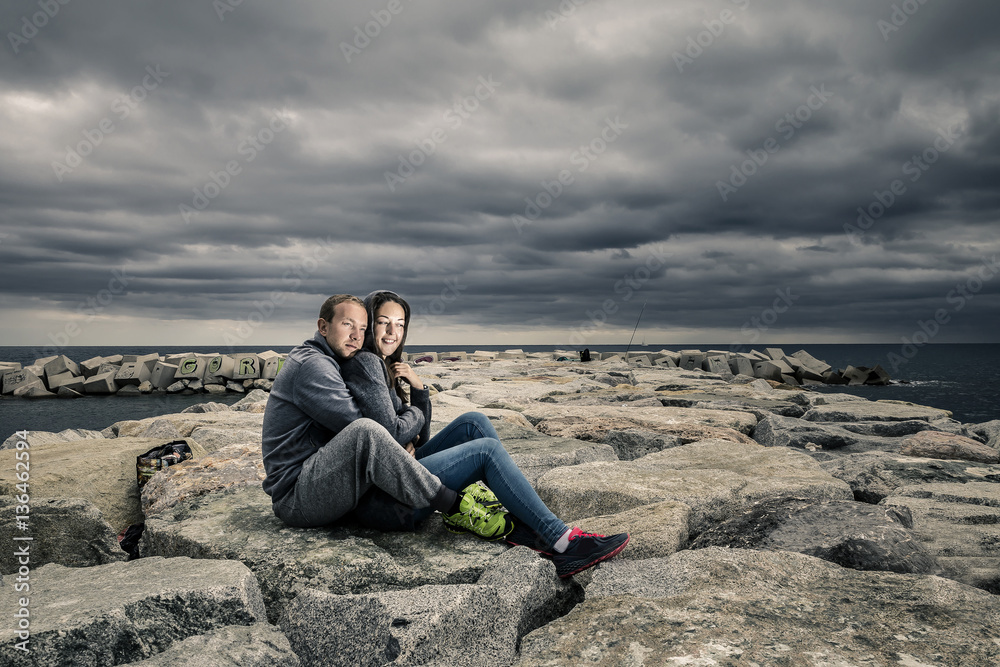 Young and attractive couple is sitting on the pier made of stone