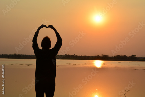 Woman put hand up beside lake under the sky and sun evening