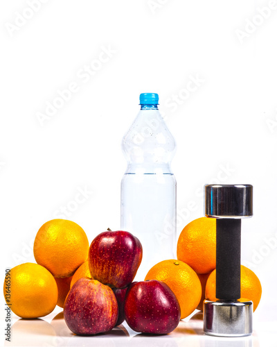 Concept of healthy active lifestyle. Red apples and oranges. Fitness dumbbell and bottle with pure drinking water between fruits. White background.