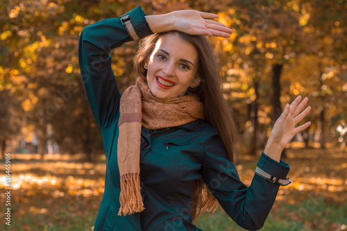 cheerful girl in Scharfe stands in autumn Park and raised her hands up