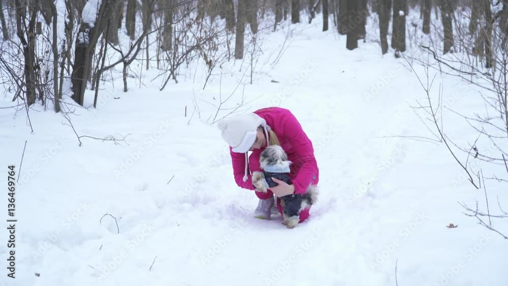 Young blonde woman playing with small dod in winter forest