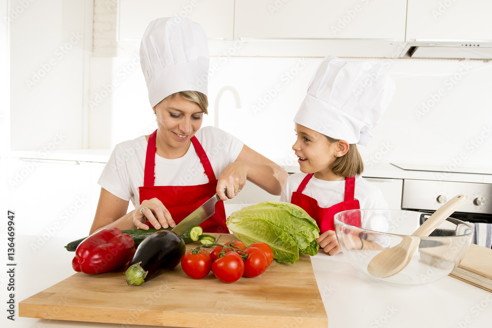 mother and little daughter cooking together with hat apron preparing salad at home kitchen mother and little daughter cooking together with hat apron preparing salad at home kitchen
