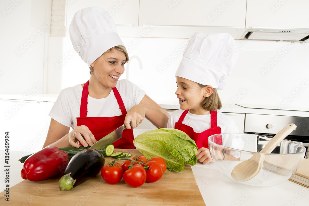mother and little daughter cooking together with hat apron preparing salad at home kitchen mother and little daughter cooking together with hat apron preparing salad at home kitchen